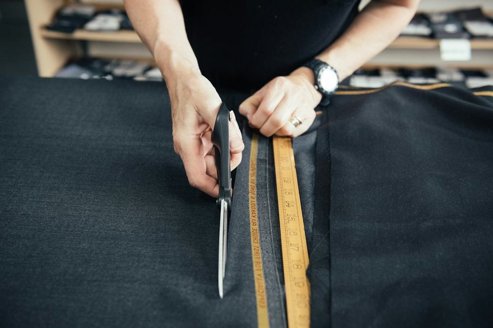 Hands cutting dark fabric with tailor's scissors along a measuring tape