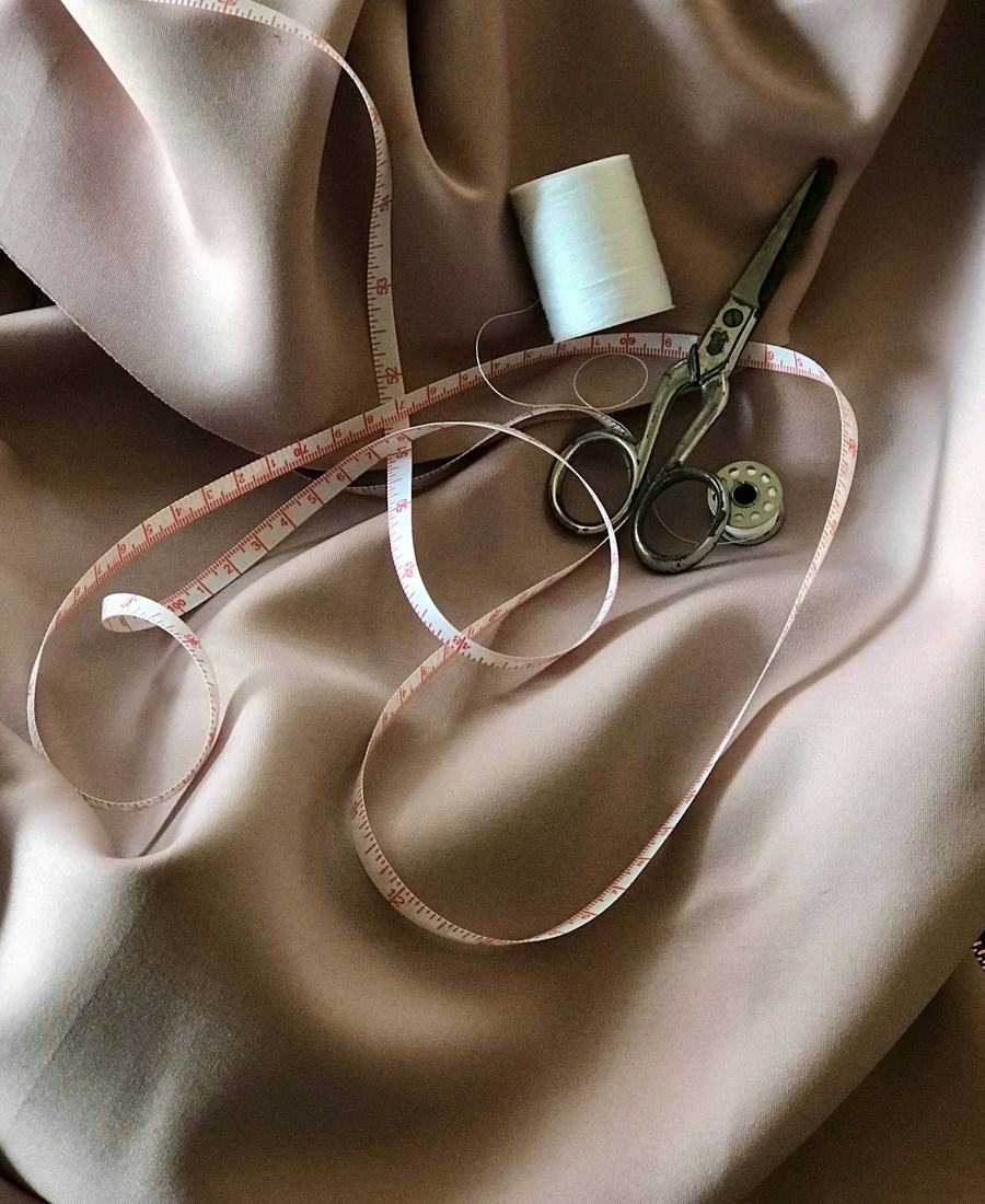 A tape measure, thread and scissors on satin fabric